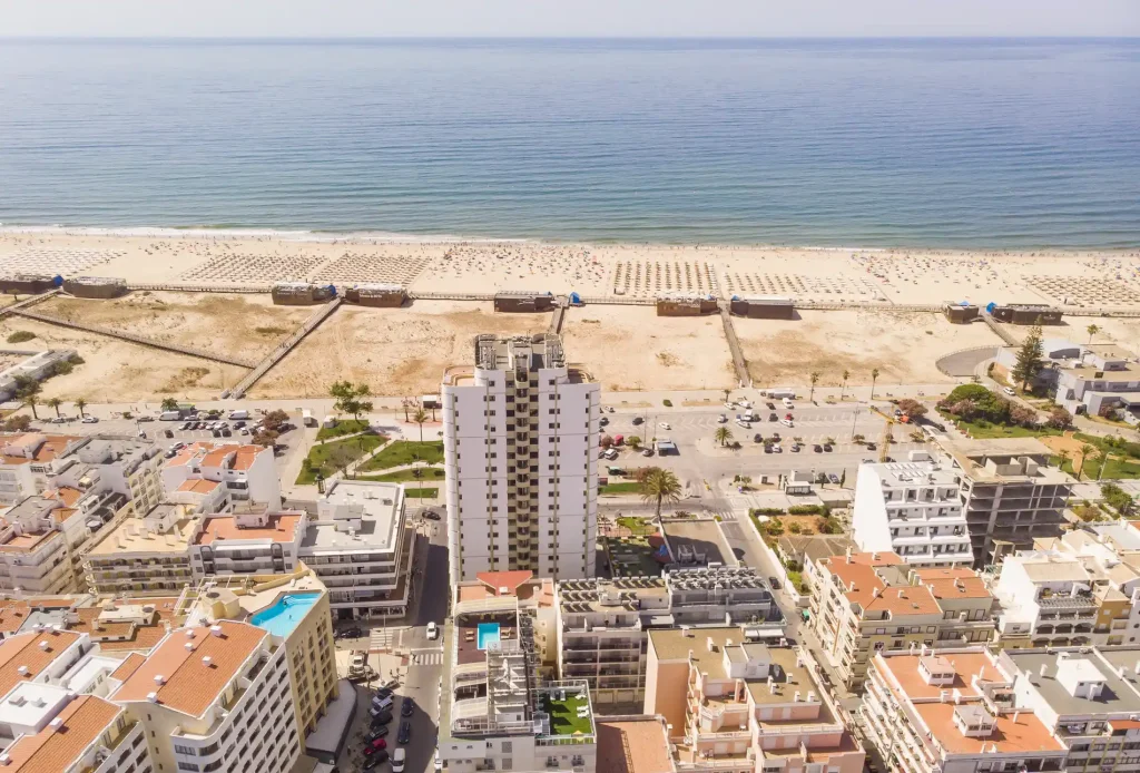 Aerial view of a coastal city with tall buildings, a beach, and the sea in the background.