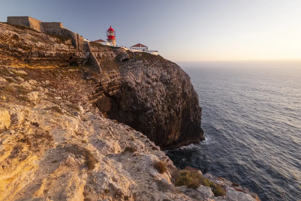 Lighthouse on a rocky cliff at sunset, overlooking the ocean.