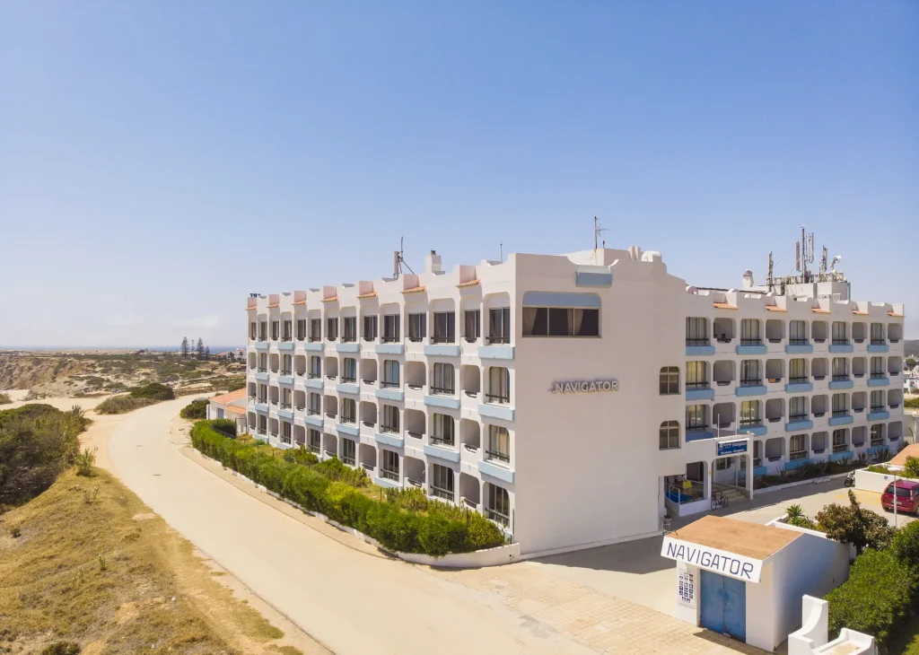 White hotel building named "Navigator" near a coastal road under a clear blue sky.