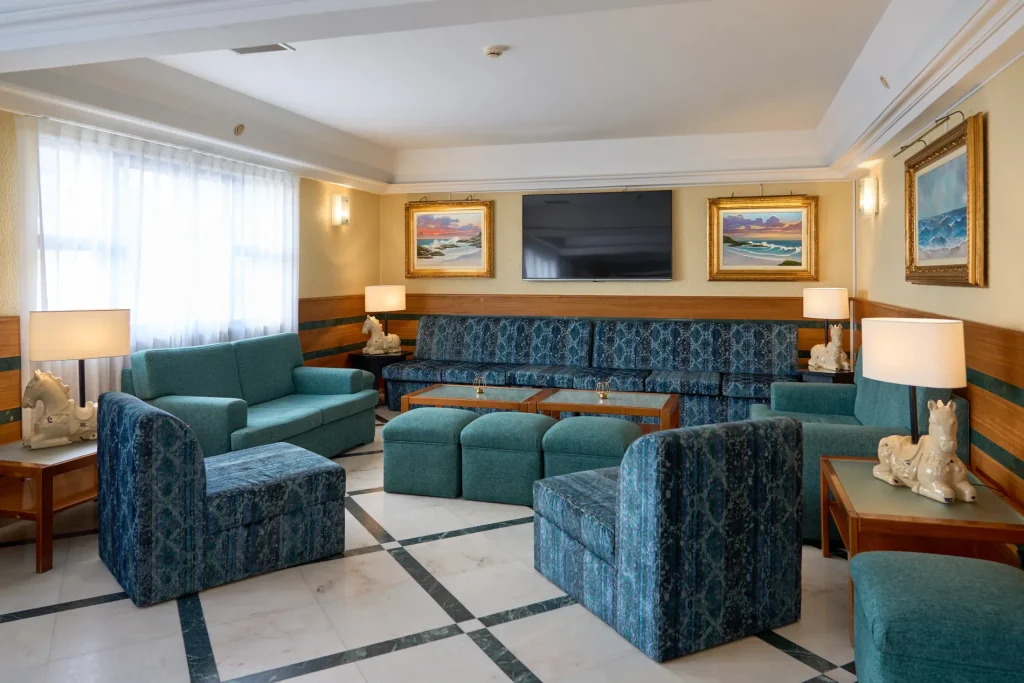 A living room with teal sofas, a TV, framed paintings, and table lamps on side tables, with horse sculptures.