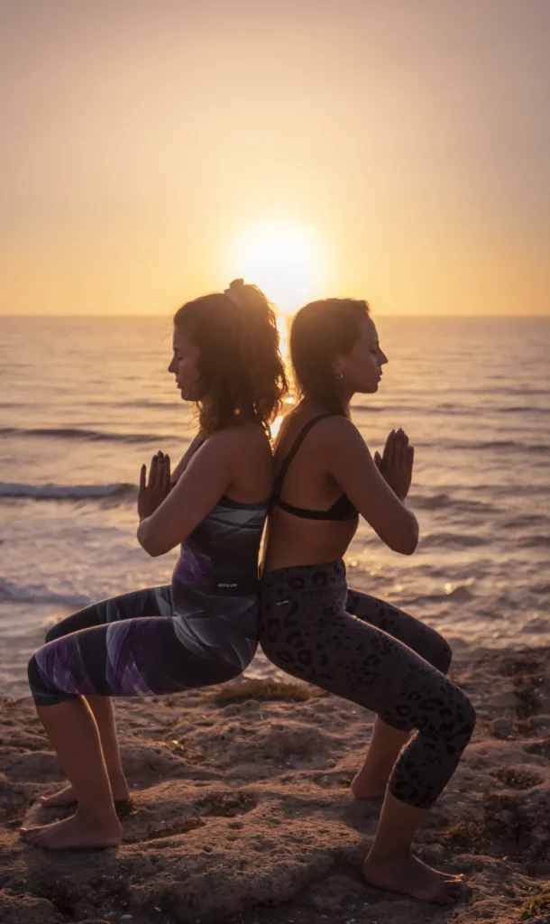 Two women practicing back-to-back yoga at sunset on a beach.