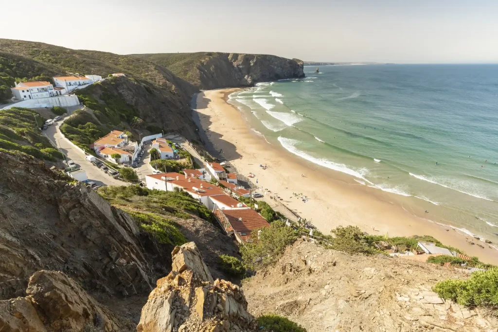 Cliffside village overlooking a sandy beach with ocean waves under a clear sky.
