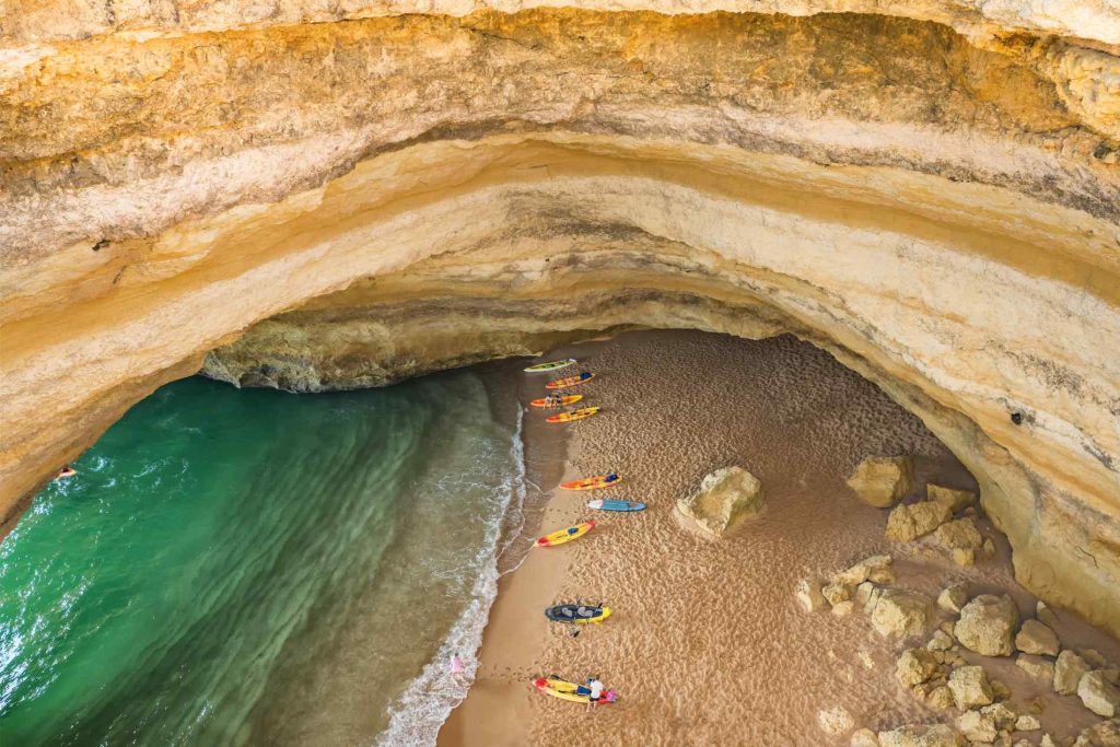 Cave beach with kayaks lined up on the sand, turquoise water, and rocky arch above.