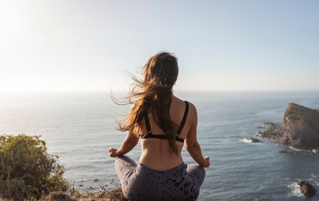 Person meditating by the ocean on a cliff edge, with wind in their hair.