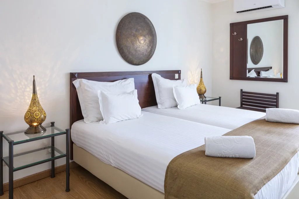 Hotel room with two twin beds, decorative lamps, circular wall art, and a mirror reflecting part of the decor.