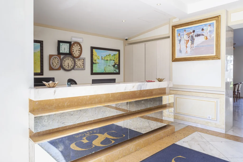 Hotel reception with marble desk, wall clocks, and paintings. Dark blue rug on the floor, elegant and inviting decor.