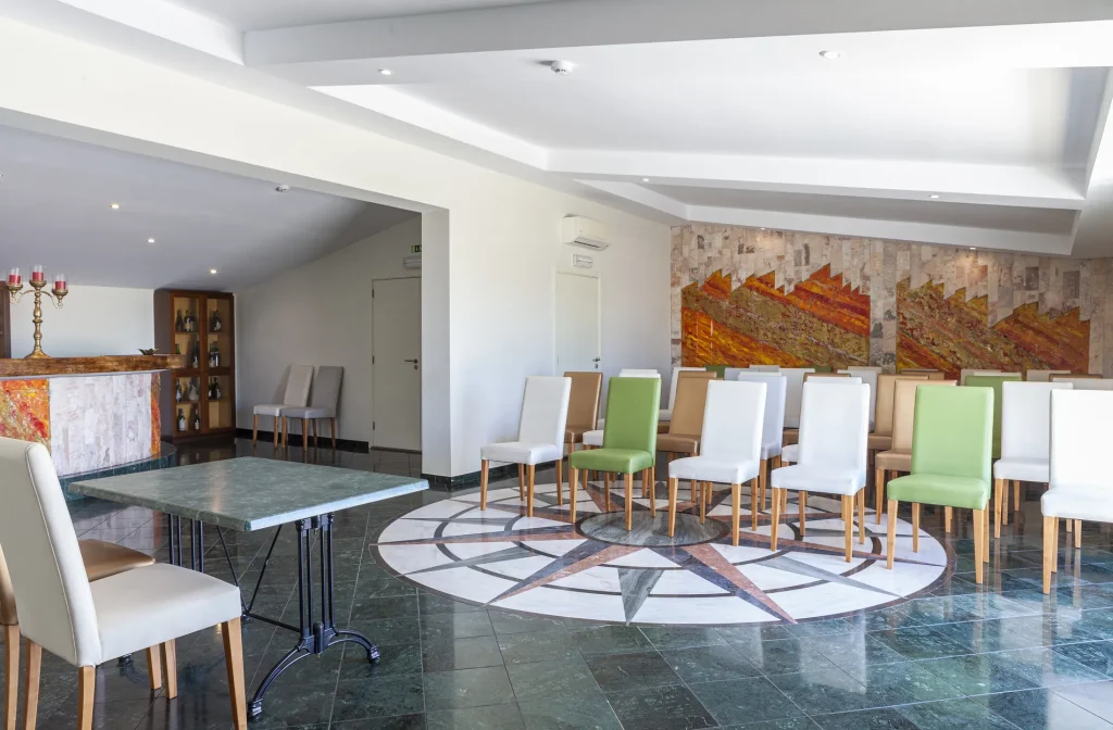 A room with arranged chairs on a circular tile pattern and a bar with shelves in the corner.