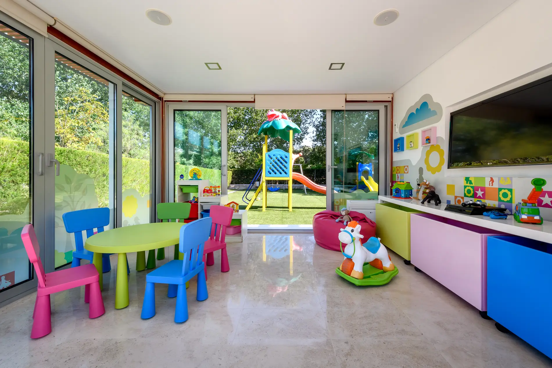 Sala de brinquedos com móveis coloridos, brinquedos e vista para o jardim com escorregador.