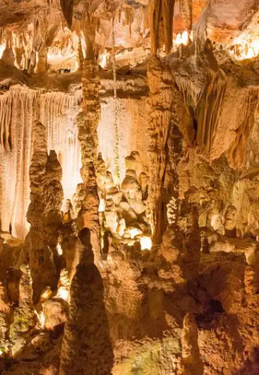 Formações de estalagmites e estalactites em caverna iluminada por luzes quentes.