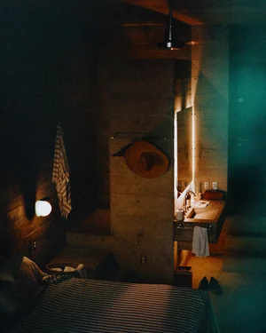 Moody room interior with a single lamp, bed, and rustic wall fixtures.