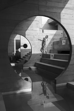Black-and-white photo of a woman walking through curved concrete arches with stairs