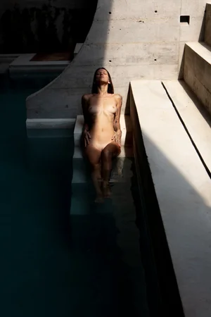 Woman standing in a sunlit pool, nude, against concrete steps