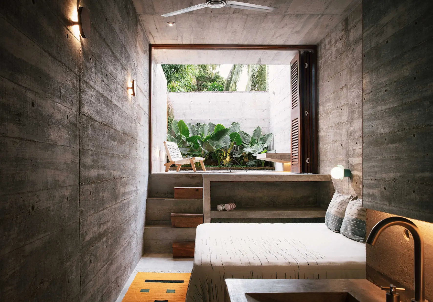 Minimalist indoor lounge with concrete walls, bench seating, and greenery view