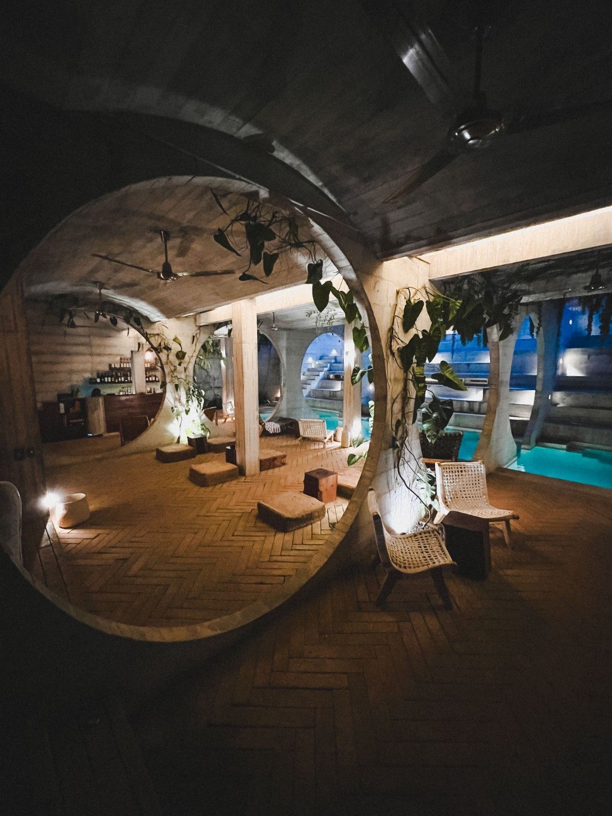 Patio interior con piscina azul, plantas colgantes y muebles de mimbre bajo techo