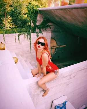 Woman in red swimsuit sitting on white pool steps with sunglasses