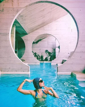 Woman in turquoise pool under circular concrete arch with greenery outside
