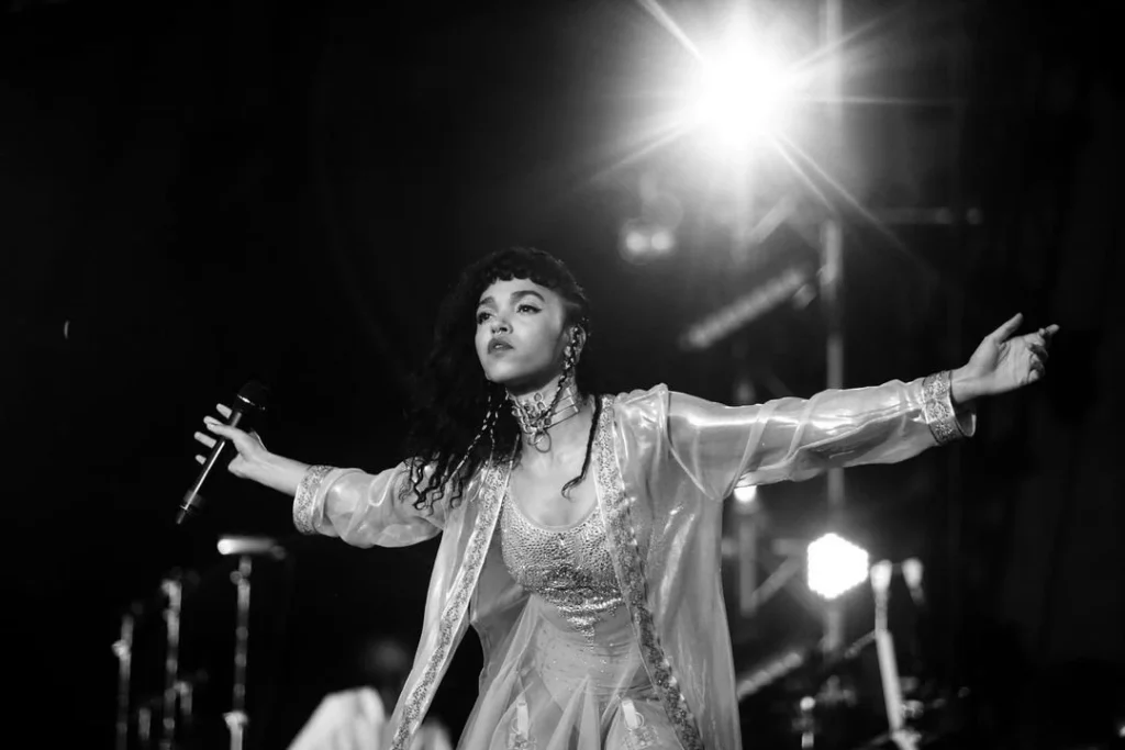 Black-and-white stage performer in sparkly costume singing with arms outstretched