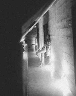Person standing in a dim hallway with concrete walls and bright light