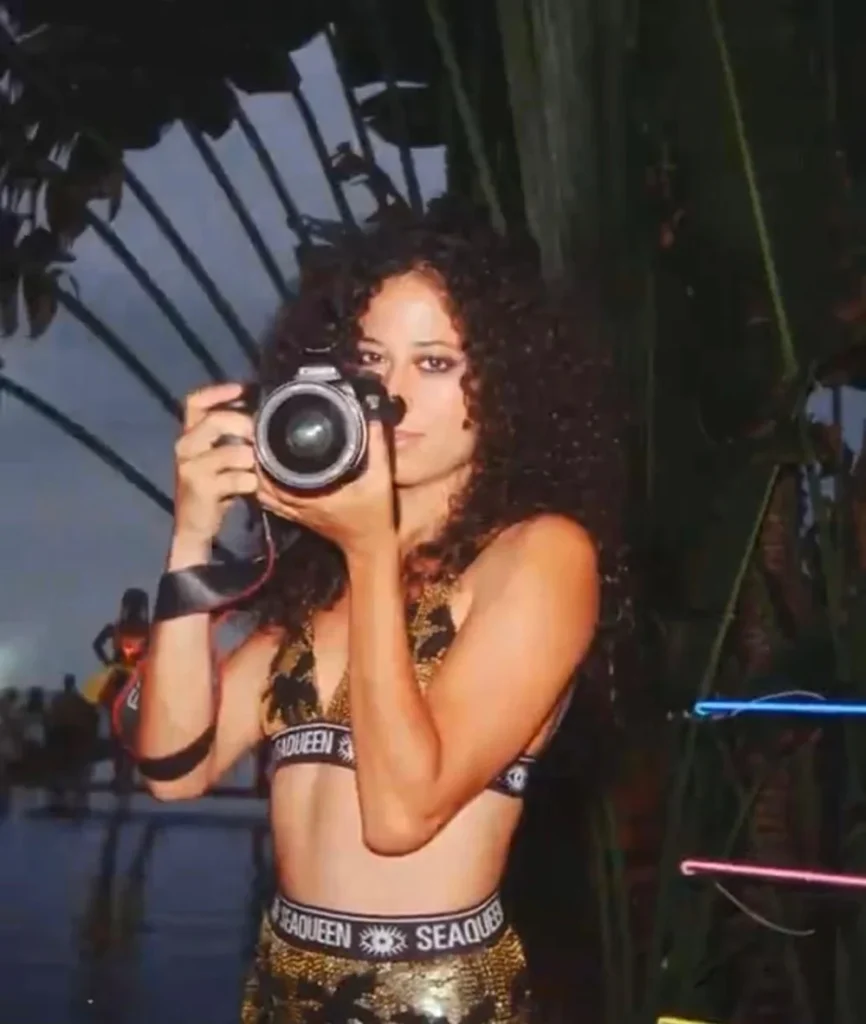 Woman in sparkly lingerie taking a mirror selfie with a camera at night