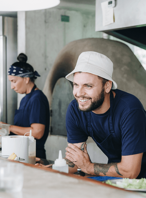 Cheerful chef in white hat working at a counter with another cook in background