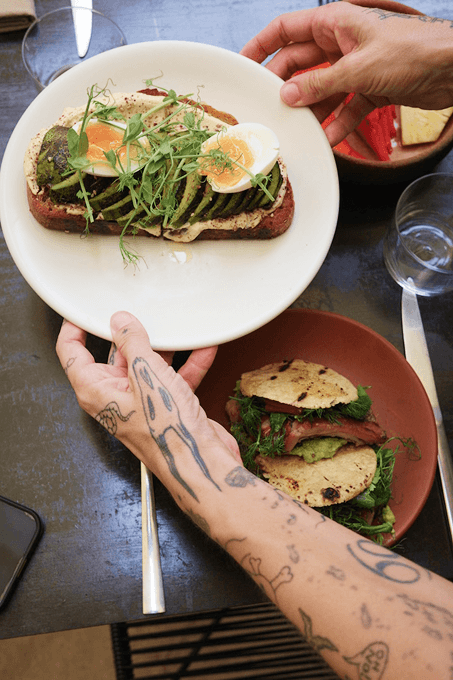 Hands placing a sandwich on plates with microgreens and grilled filling