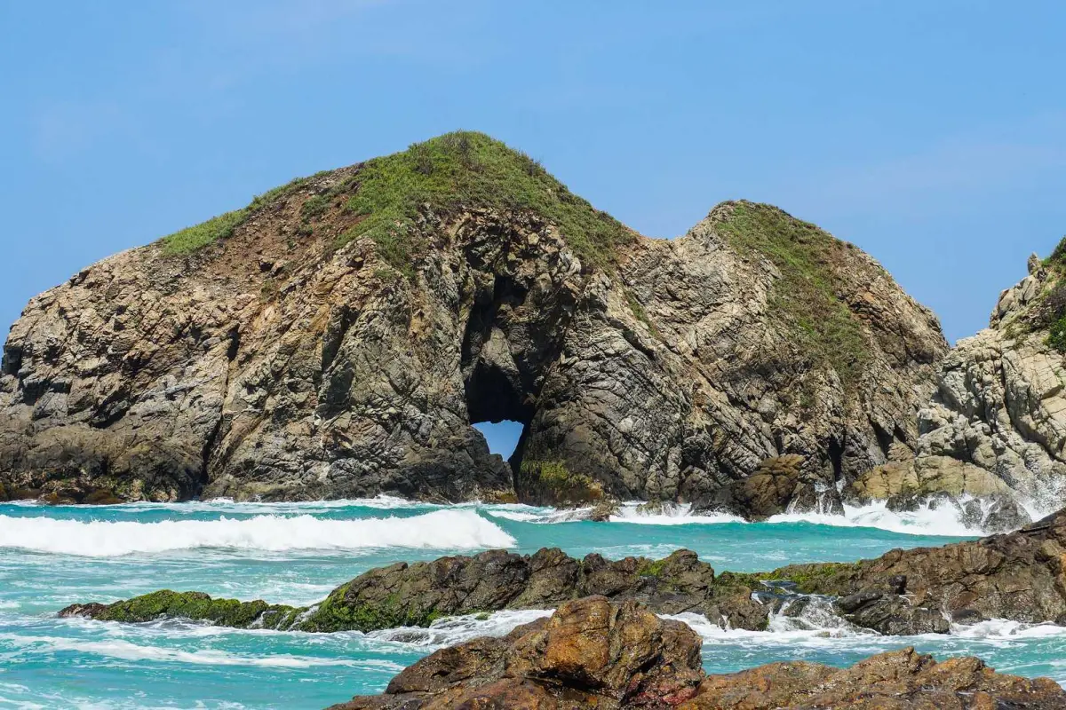 Rugged sea cliffs with a cave opening above turquoise waves and surf