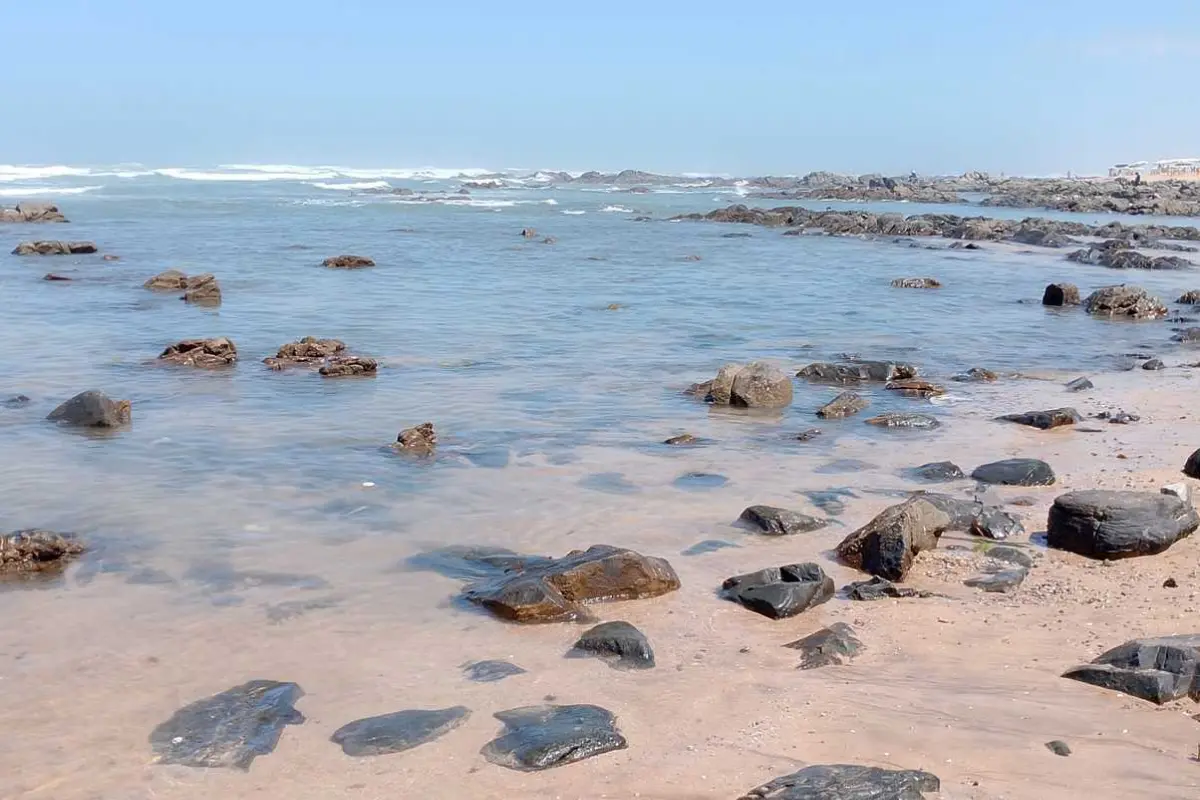 Rocky shoreline with ocean waves and scattered stones on a sandy beach