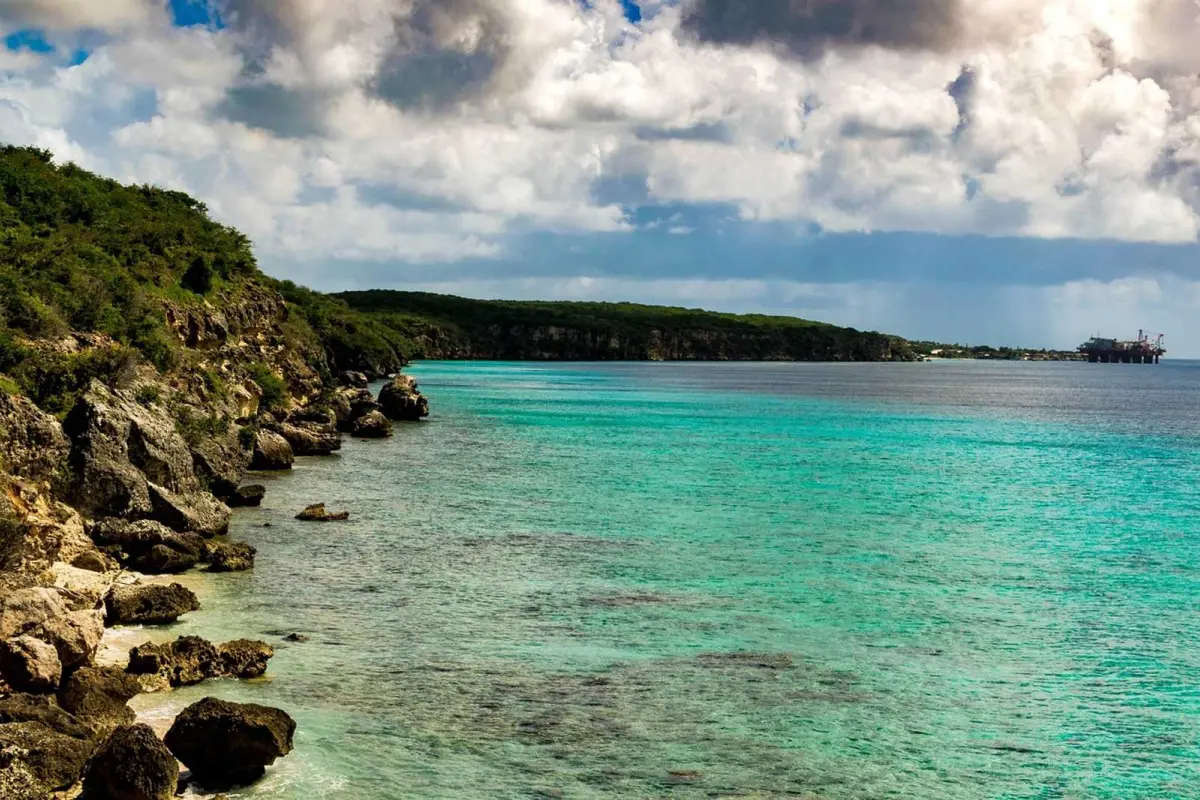 Turquoise ocean along a rocky coastline with clouds and distant ship in view