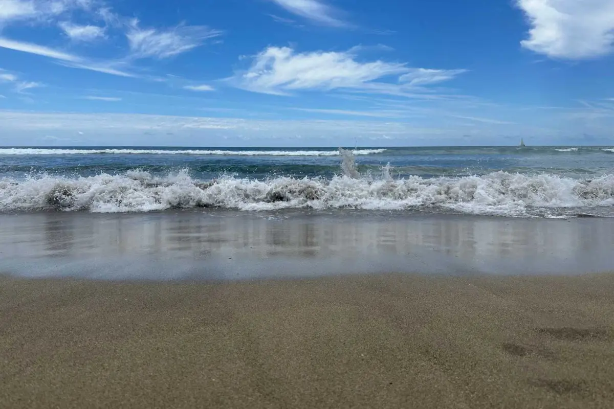 Waves crash on a sandy beach under a blue sky with scattered clouds
