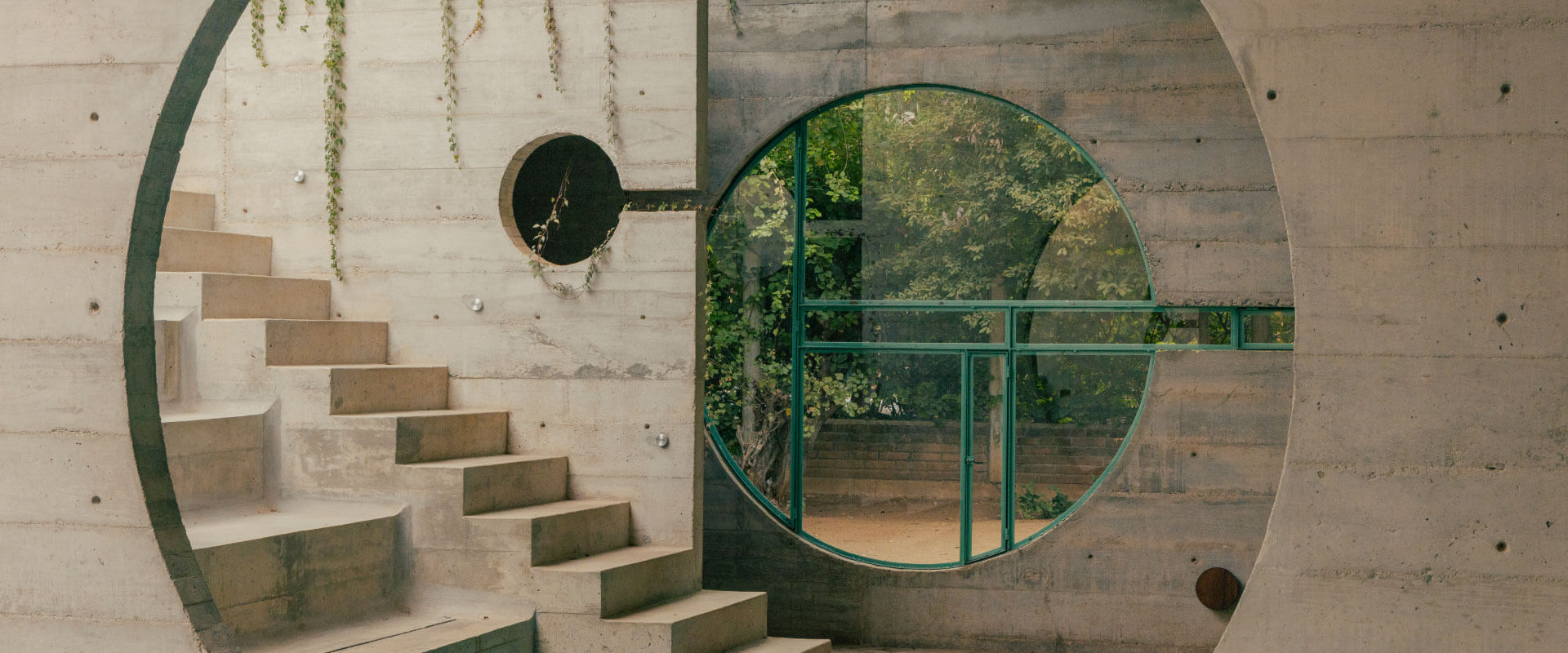 Staircase and circular green-framed window in a concrete courtyard with vines