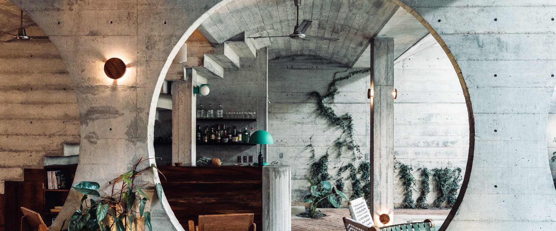 Interior of a concrete bar with shelves, plants, and hanging lamps