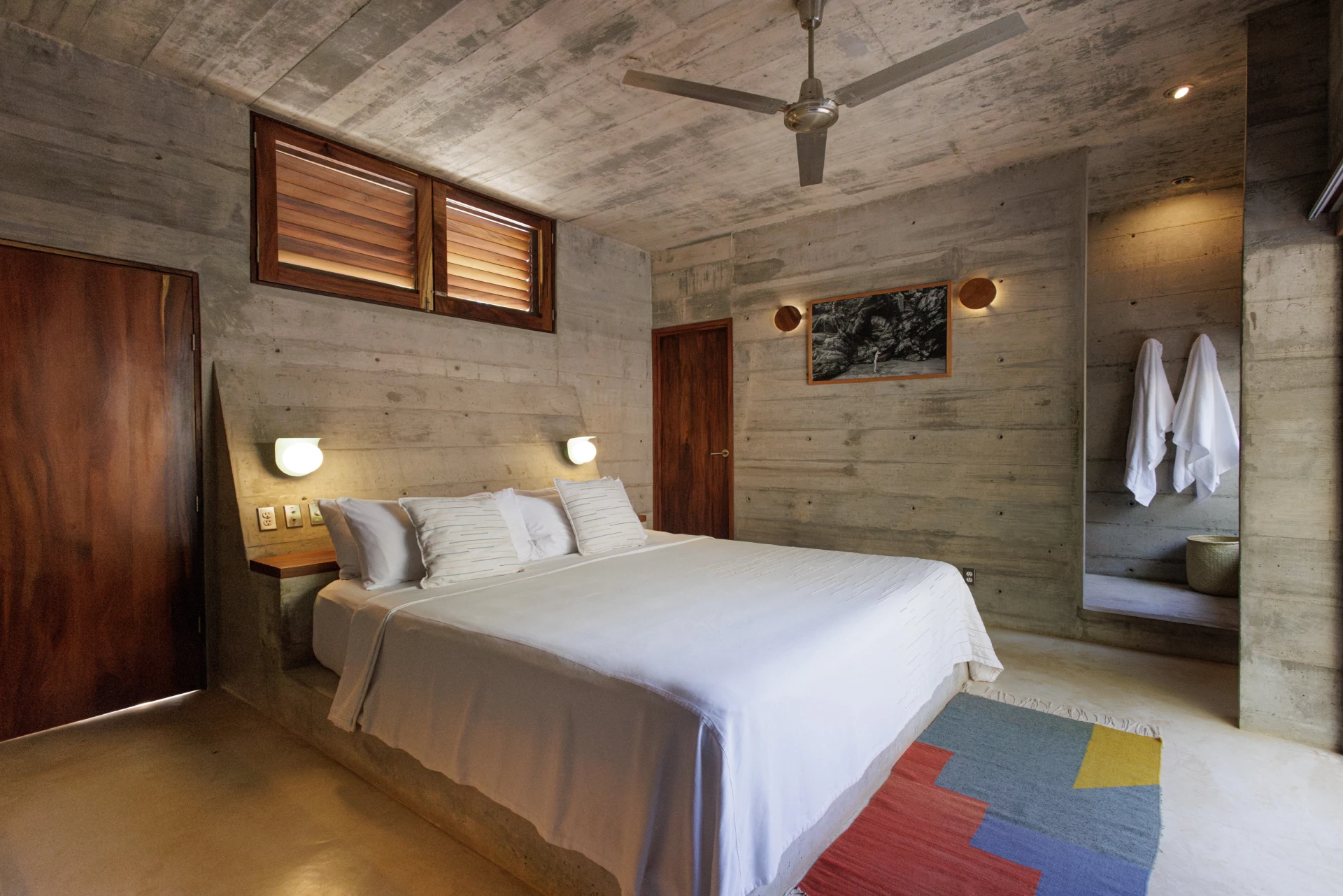 Modern bedroom with concrete walls, ceiling fan, and a white bed setup