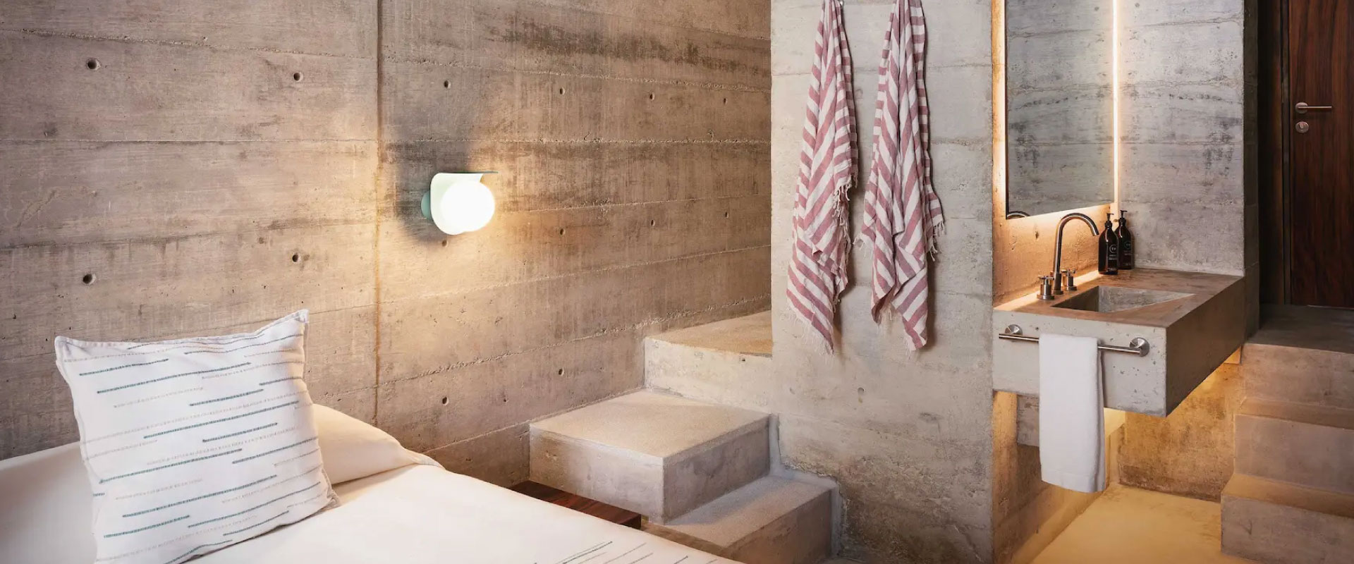 Modern concrete bathroom with sink, towels, light, and bed-like seating bench