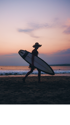 Surfista con tabla de surf al atardecer en la playa con nubes.