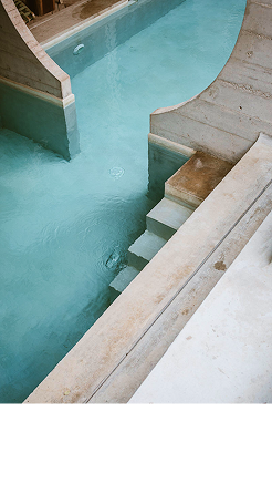 Piscina de agua turquesa con escalones de piedra y borde verde.