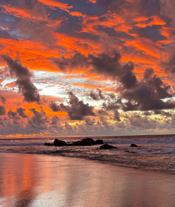 Atardecer con nubes dramáticas y olas rompiendo en una playa con rocas.