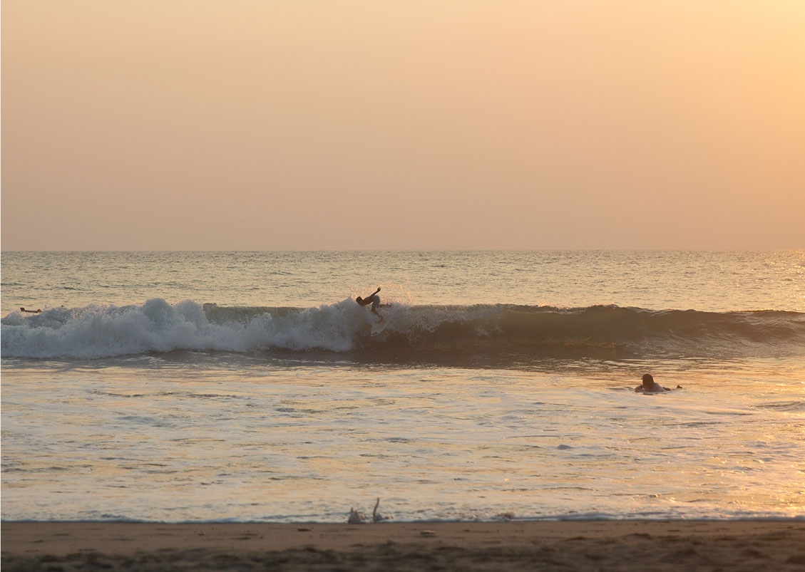 Surfer catching a wave at sunset with golden ocean spray and sky