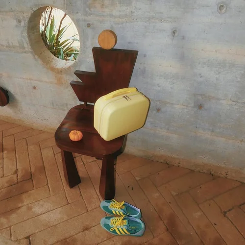 Wooden statue with head on pedestal and yellow bag by shoes against wall