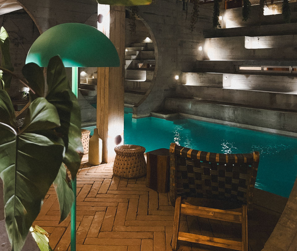 Interior con piscina turquesa y luces cálidas, junto a una mesa de madera.