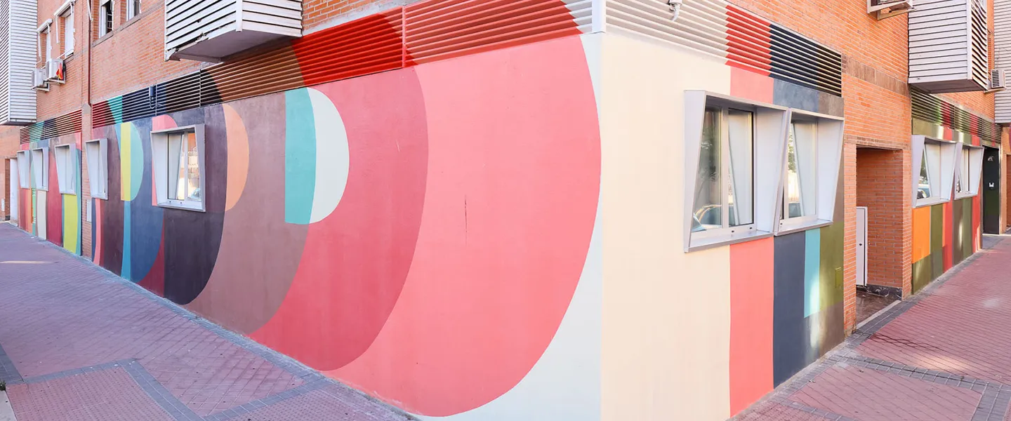 Fachada de edificio con mural geométrico en colores vivos y ventanas rectangulares abiertas a la calle.