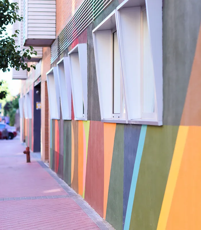 Edificio con ventanas inclinadas y un mural de colores geométricos en la pared lateral.