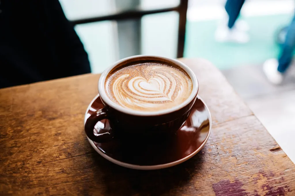 Taza de café con arte de leche en forma de corazón sobre una mesa de madera.