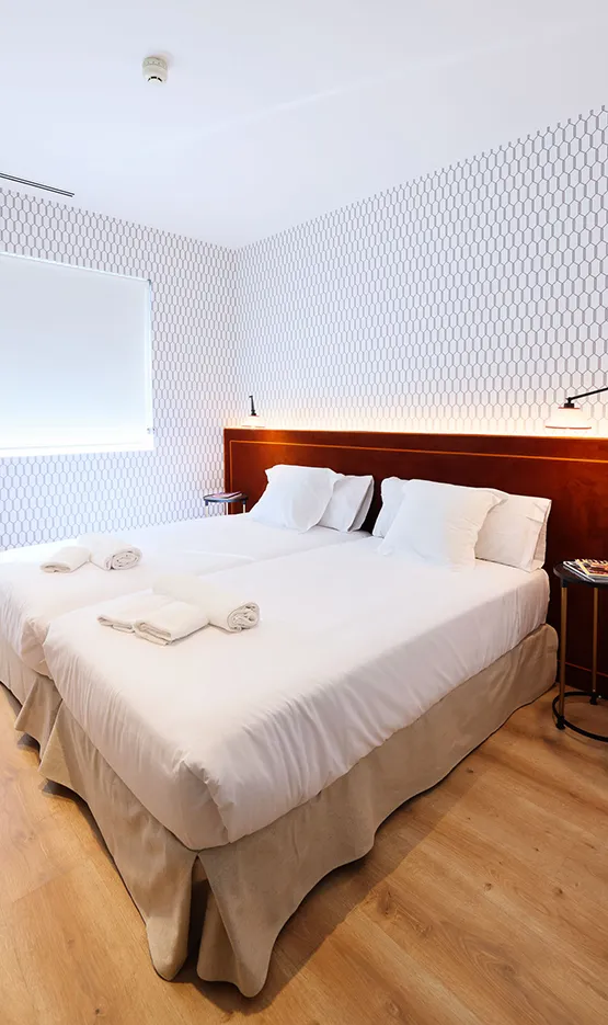 Habitación moderna con dos camas individuales, paredes con diseño geométrico, y suelo de madera clara.