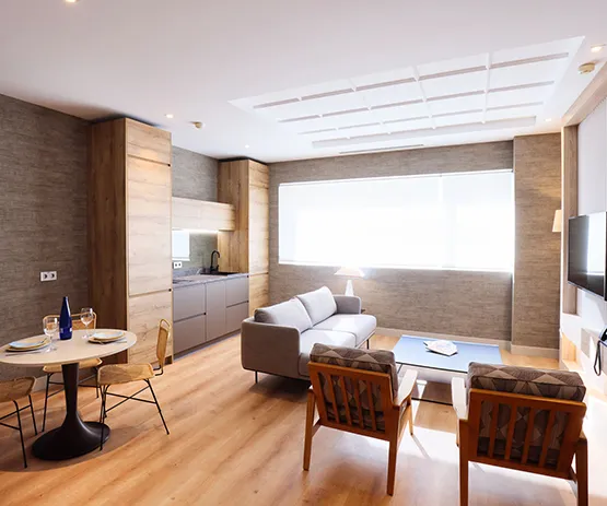 Sala de estar moderna con sofá, cocina integrada, mesa de comedor y sillas; decoración en tonos neutros y madera.