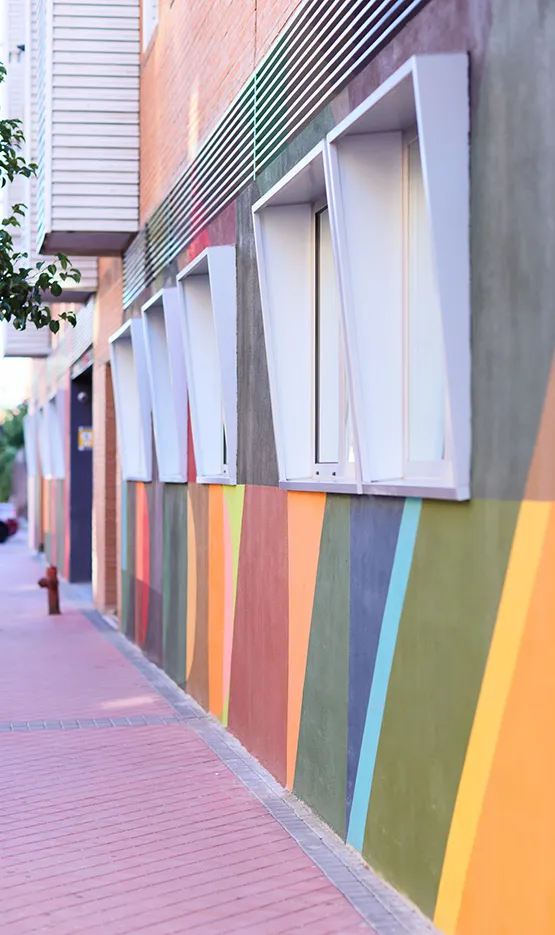 Fachada de edificio con ventanas modernas y pared decorada con líneas diagonales de colores brillantes.
