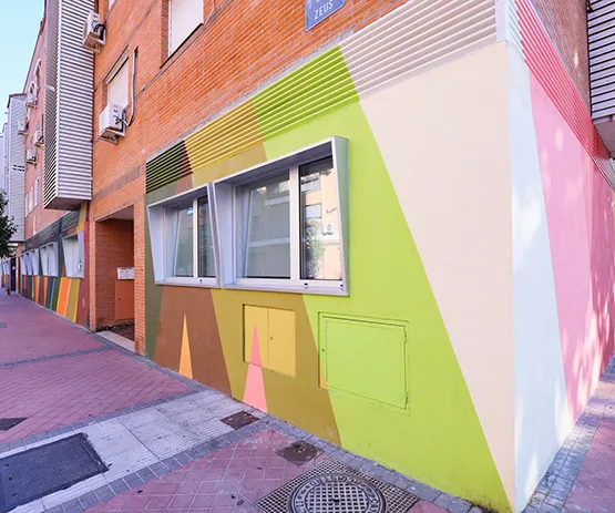 Fachada colorida de edificio con patrones geométricos en tonos pastel, ventanas grandes y acera de ladrillo.