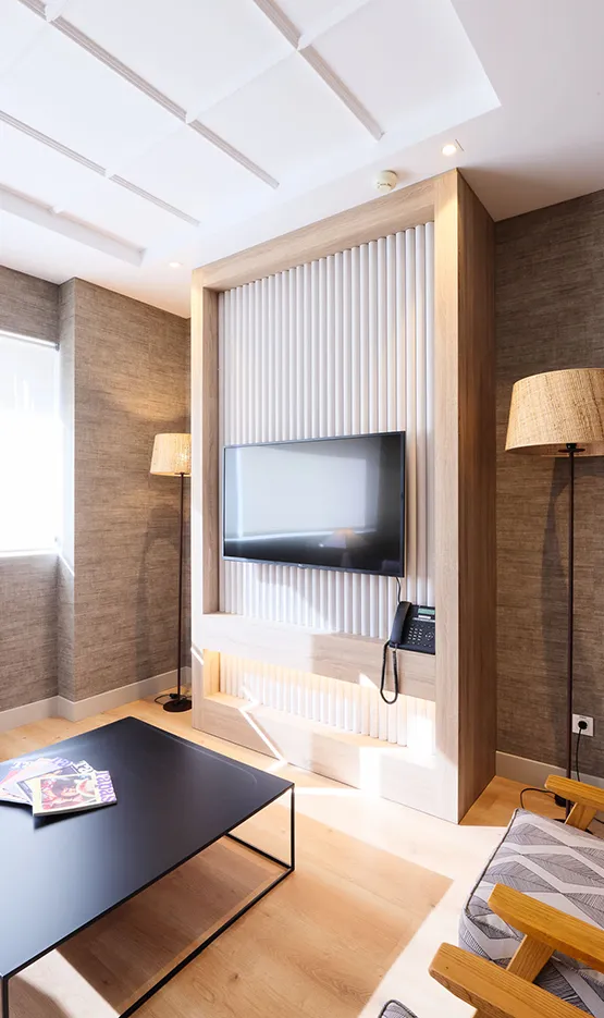 Sala moderna con televisor empotrado, lámparas de pie, mesa negra y sofá gris. Decoración elegante y luminosa.