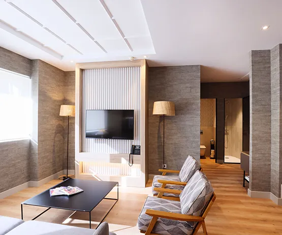 Sala moderna con muebles minimalistas, dos sillas, mesa central, lámparas y televisor en la pared oscura.