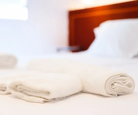 Toallas blancas enrolladas sobre una cama blanca, con un cabecero de madera al fondo.