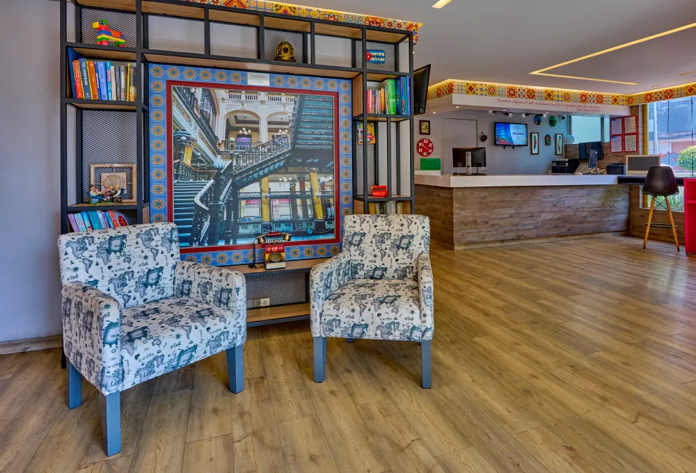 Sala moderna con sillas tapizadas y librero, junto a un &aacute;rea de recepci&oacute;n de hotel.